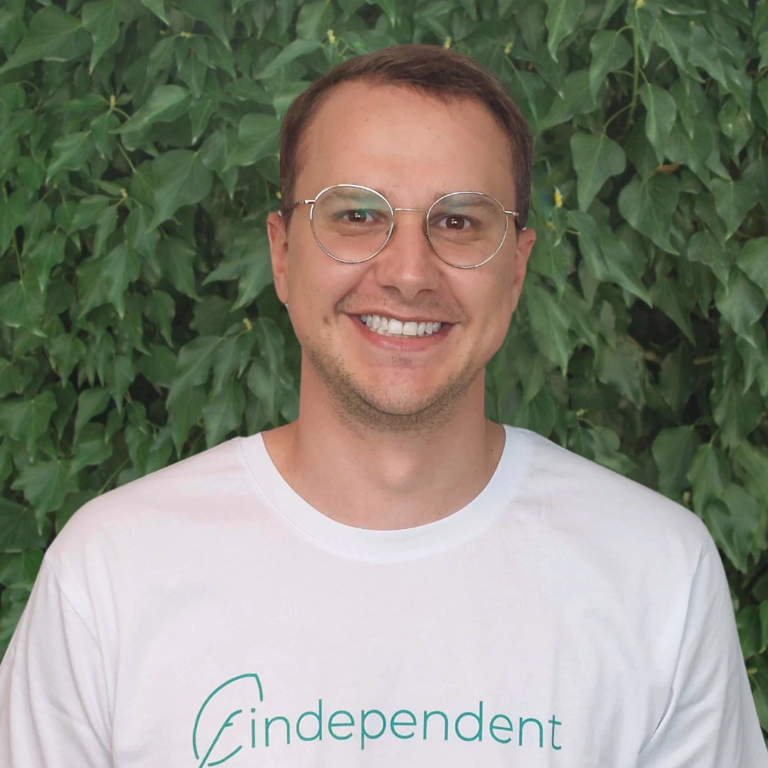 Ein Mann, Tobias K von findependent., steht vor einem Hintergrund aus grünen Blättern